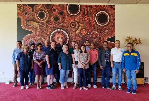 Group of people posing for photo in front of a large Indigenous artwork.