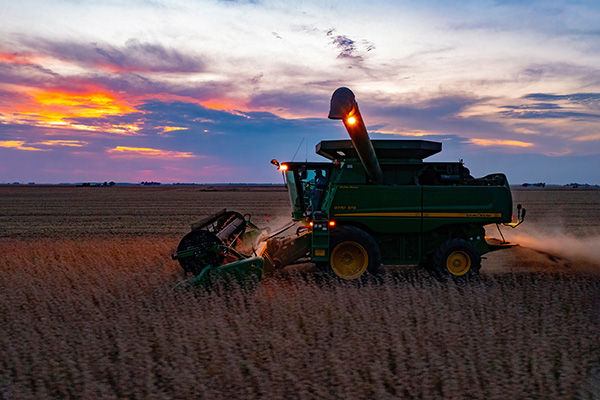 A harvester working in a paddock as the sun goes down in the background