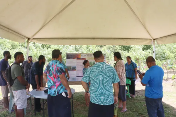 People gathered under an outdoor marquee looking at a poster presentation.