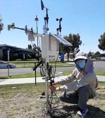 masked researcher crouched next to fancy climate station