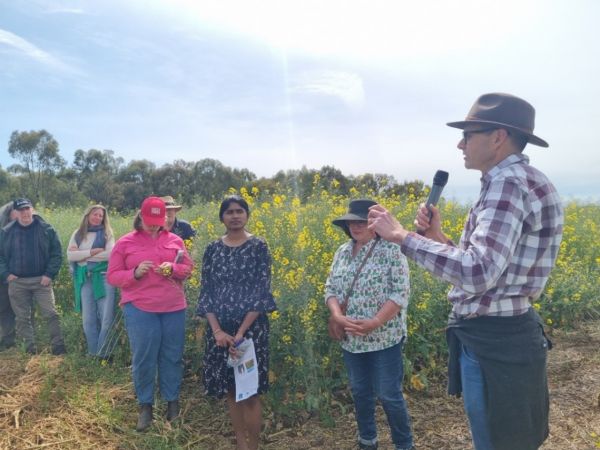 Prof James Hunt holds a microphone and presents to a group of people standing in a paddock.