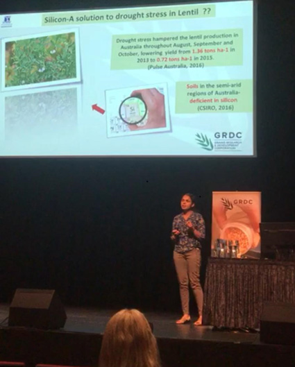 Dr Sajitha Biju presenting on stage with a large screen behind her.