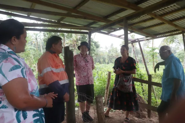 People standing under a shelter near a field of crops.
