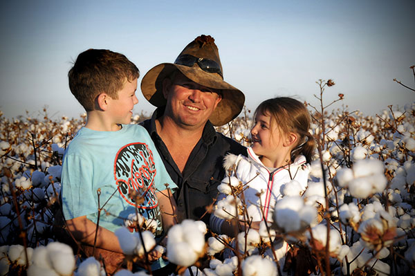 Man standing in cotton field with two children