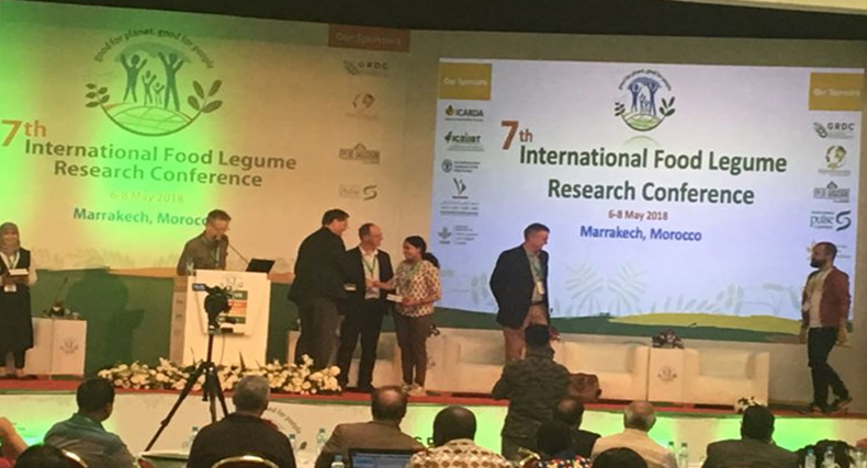Dr Sajitha Biju on stage shaking hands with dignitaries, accepting the award for best poster presentation. 