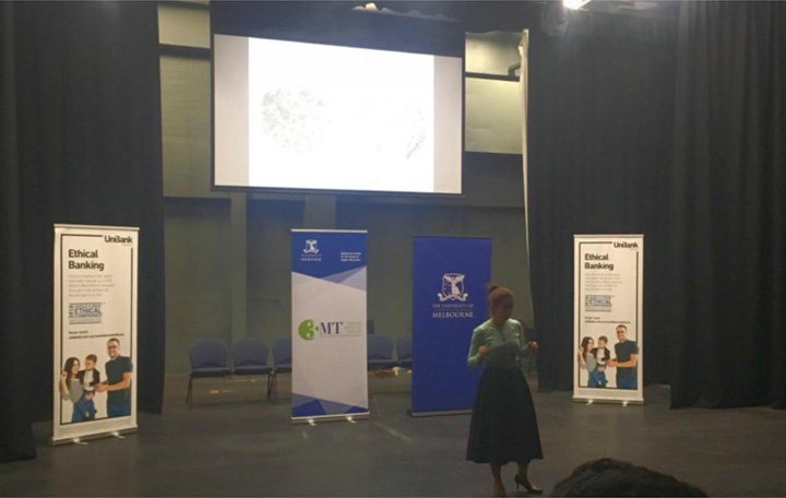 Dr. Mahya Tawan standing presenting in front of a large projector screen